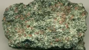 Close-up photograph of a red-and-green eclogite rock specimen with garnet crystals embedded in metamorphic minerals