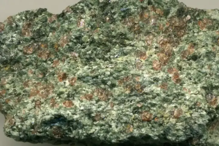 Close-up photograph of a red-and-green eclogite rock specimen with garnet crystals embedded in metamorphic minerals