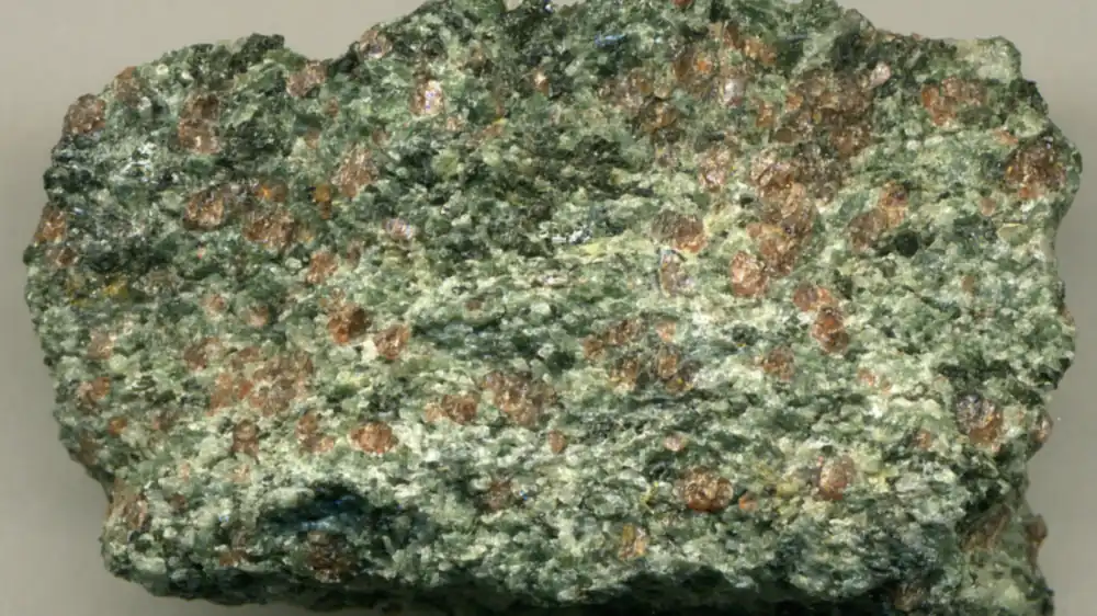 Close-up photograph of a red-and-green eclogite rock specimen with garnet crystals embedded in metamorphic minerals
