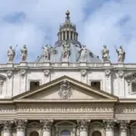 Wide exterior view of the facade and papal balcony of St. Peter’s Basilica overlooking St. Peter’s Square in Vatican City.