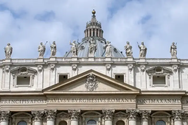 Wide exterior view of the facade and papal balcony of St. Peter’s Basilica overlooking St. Peter’s Square in Vatican City.