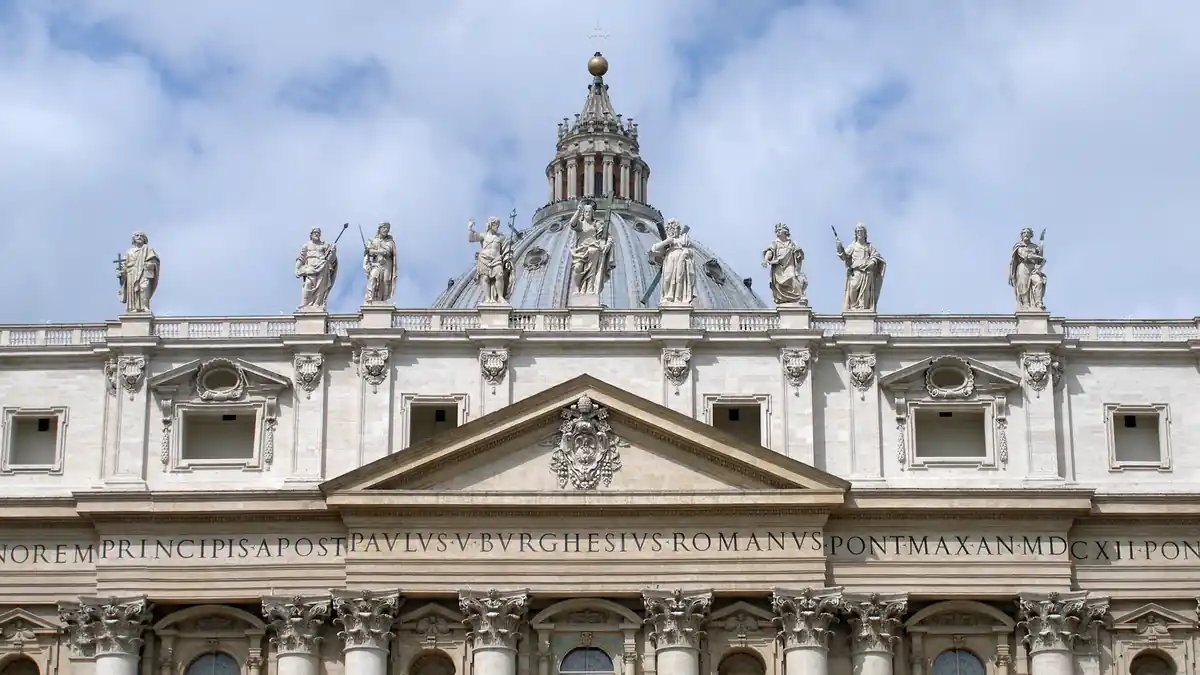 Wide exterior view of the facade and papal balcony of St. Peter’s Basilica overlooking St. Peter’s Square in Vatican City.