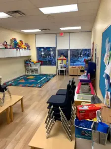 Clean and structured early childhood preschool classroom showing small activity tables, educational toys, and learning stations.