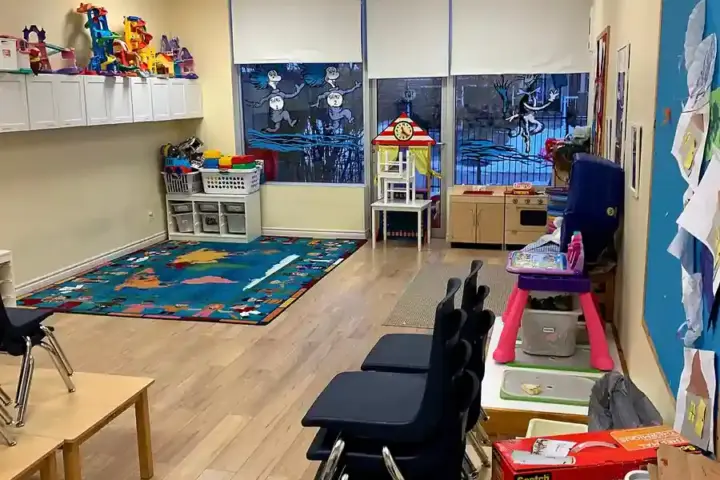 Clean and structured early childhood preschool classroom showing small activity tables, educational toys, and learning stations.