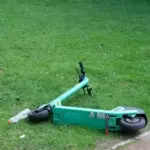 Green e-scooter lying beside a paved park path, showing a personal mobility device without visible branding