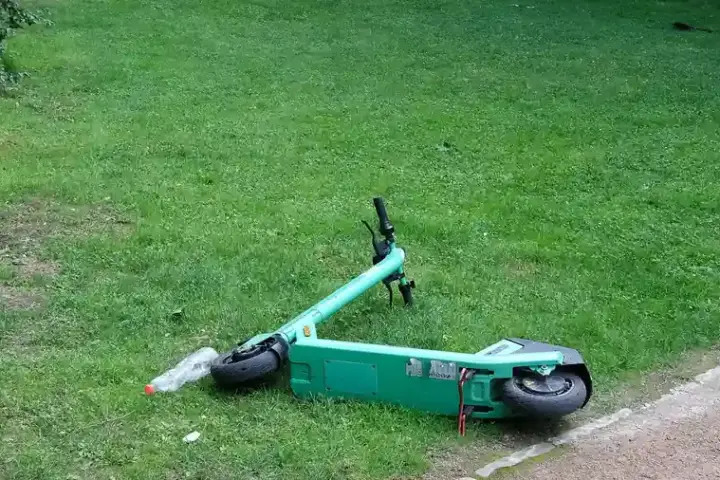 Green e-scooter lying beside a paved park path, showing a personal mobility device without visible branding
