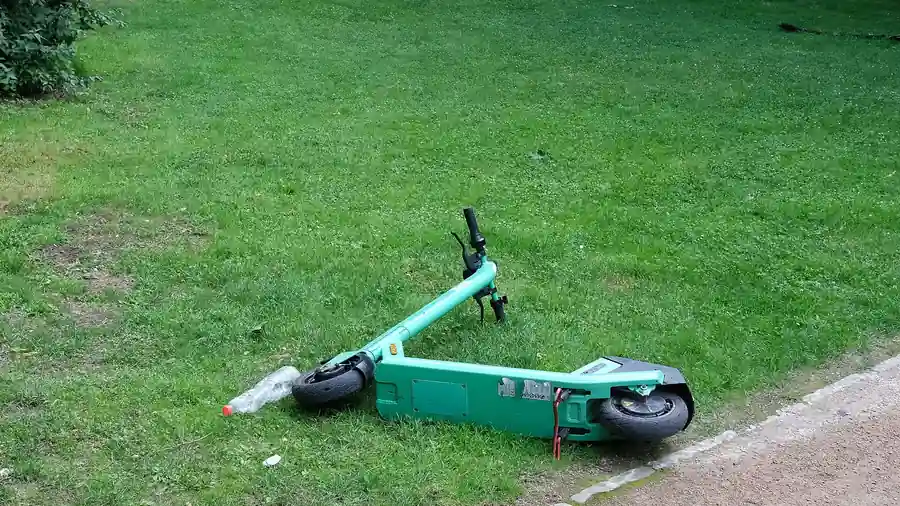 Green e-scooter lying beside a paved park path, showing a personal mobility device without visible branding