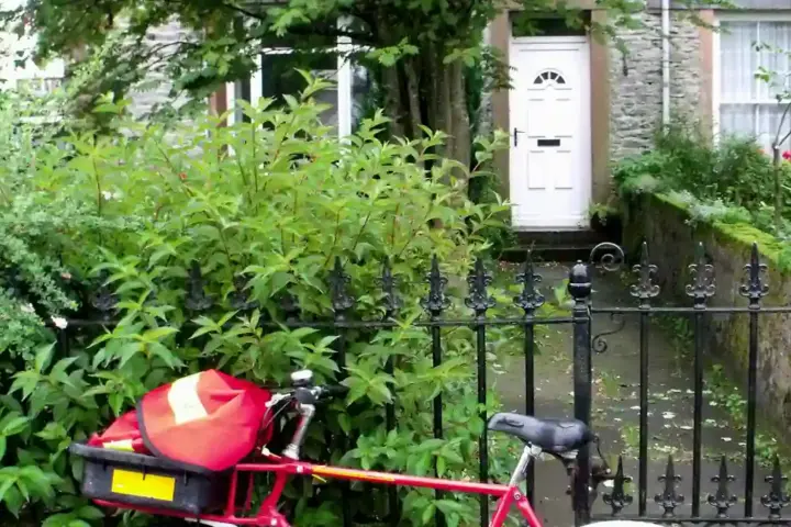 A postal worker on a bicycle with mailbag delivering mail to a residential street with a warning sign