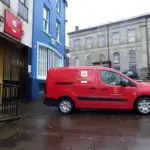 Red postal-delivery van parked on a UK street