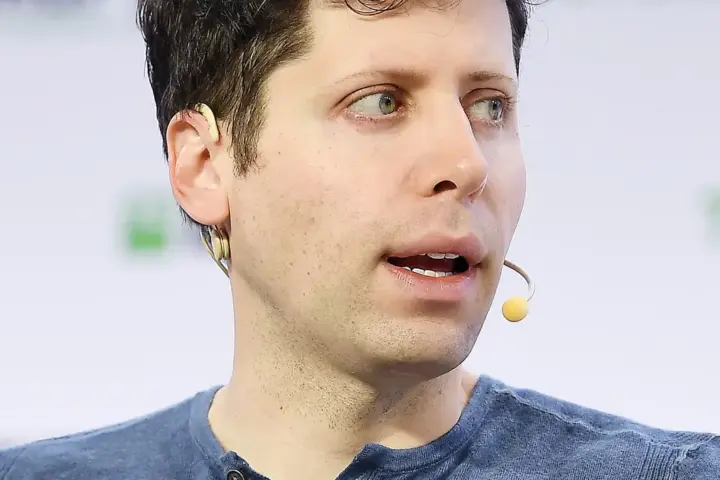 Sam Altman at a podium speaking at a technology conference, gesturing with hands to the audience