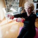An older adult using elastic resistance bands to perform an upper-body strength exercise indoors.