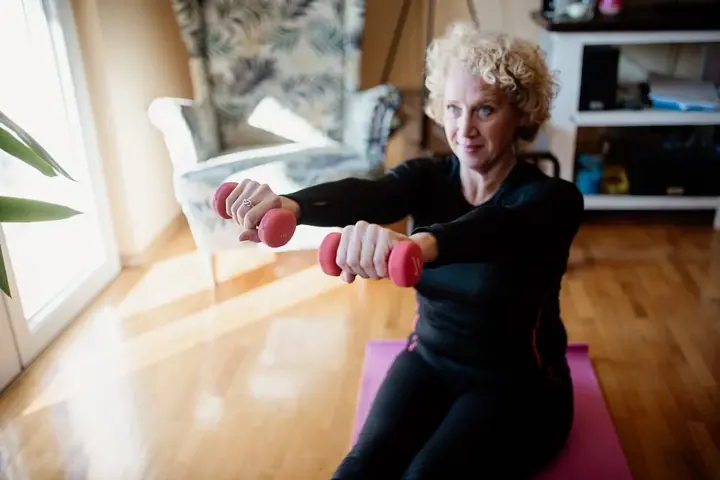 An older adult using elastic resistance bands to perform an upper-body strength exercise indoors.