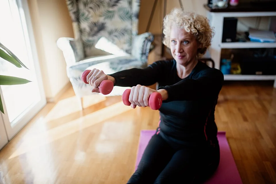 An older adult using elastic resistance bands to perform an upper-body strength exercise indoors.