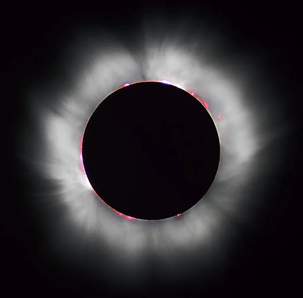 High-contrast astronomical photograph capturing totality during a solar eclipse, with the black silhouette of the Moon surrounded by glowing white coronal streamers.
