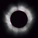 High-contrast astronomical photograph capturing totality during a solar eclipse, with the black silhouette of the Moon surrounded by glowing white coronal streamers.