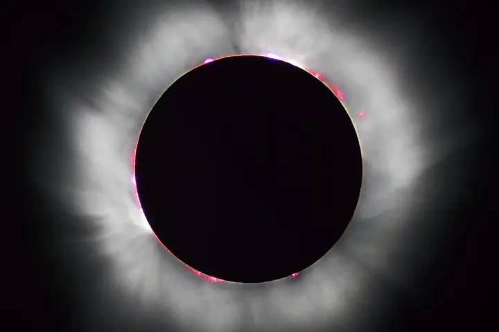 High-contrast astronomical photograph capturing totality during a solar eclipse, with the black silhouette of the Moon surrounded by glowing white coronal streamers.