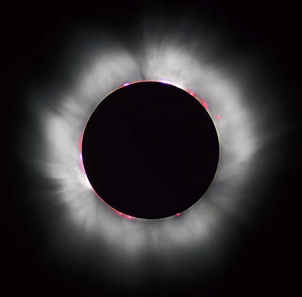 High-contrast astronomical photograph capturing totality during a solar eclipse, with the black silhouette of the Moon surrounded by glowing white coronal streamers.