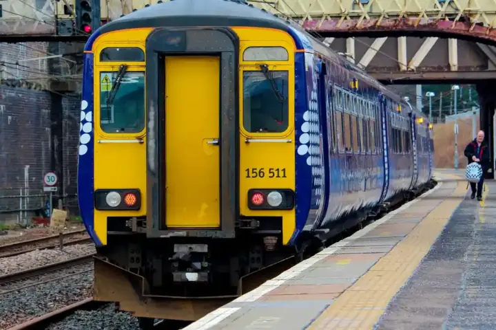 A blue and white ScotRail Sprinter passenger train standing on wet railway tracks at Carstairs Railway Station in Scotland.