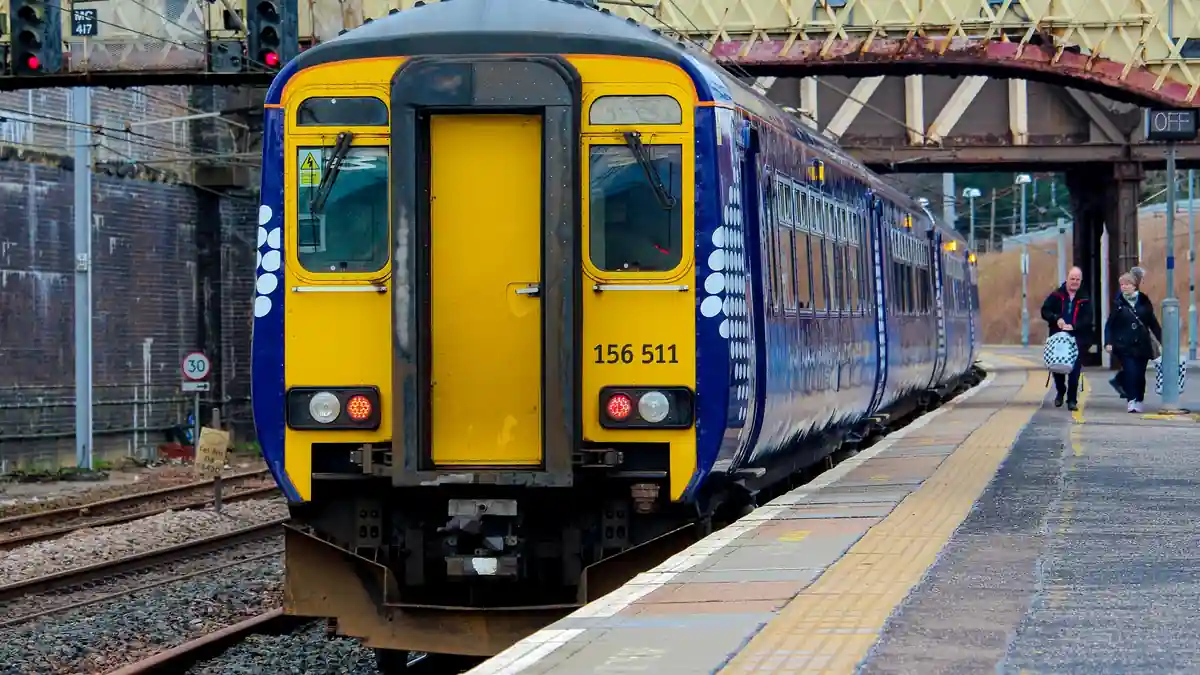 A blue and white ScotRail Sprinter passenger train standing on wet railway tracks at Carstairs Railway Station in Scotland.