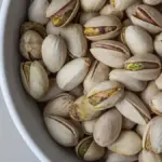 Close-up photograph of whole shelled pistachio nuts in bulk storage prior to commercial packaging and distribution.