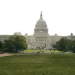 Full architectural photograph of the United States Capitol building under clear daylight, displaying the central dome and legislative wings.