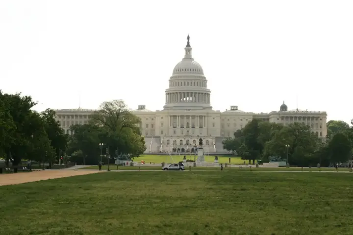 Full architectural photograph of the United States Capitol building under clear daylight, displaying the central dome and legislative wings.