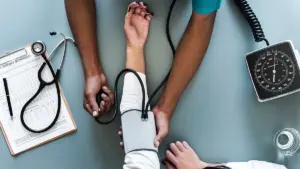 Blood pressure monitoring gauge and inflatable arm cuff resting on a wooden examination table in a clinical setting.