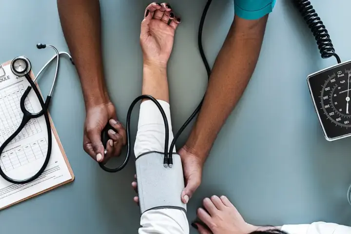 Blood pressure monitoring gauge and inflatable arm cuff resting on a wooden examination table in a clinical setting.