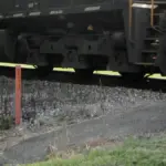 Close-up of freight train bogies and wheels beside a rural rail crossing signal post