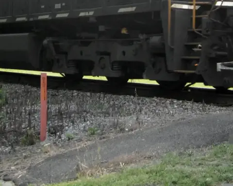 Close-up of freight train bogies and wheels beside a rural rail crossing signal post