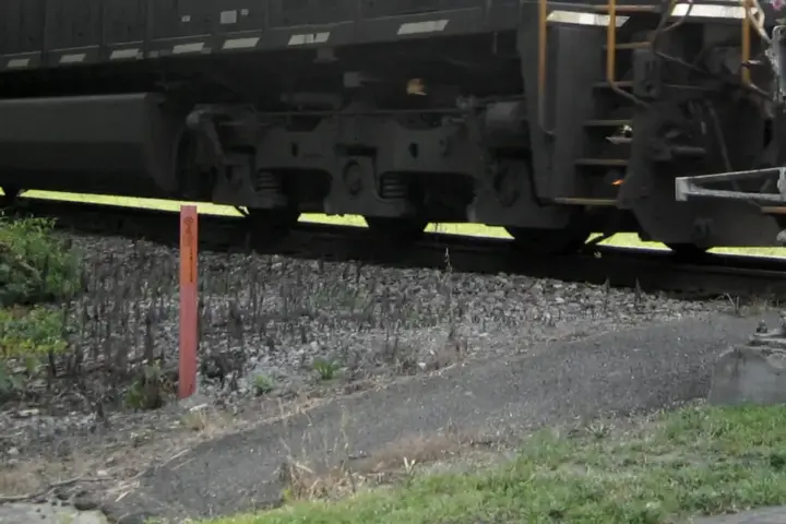 Close-up of freight train bogies and wheels beside a rural rail crossing signal post