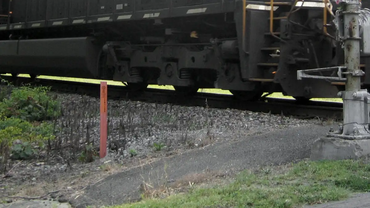 Close-up of freight train bogies and wheels beside a rural rail crossing signal post