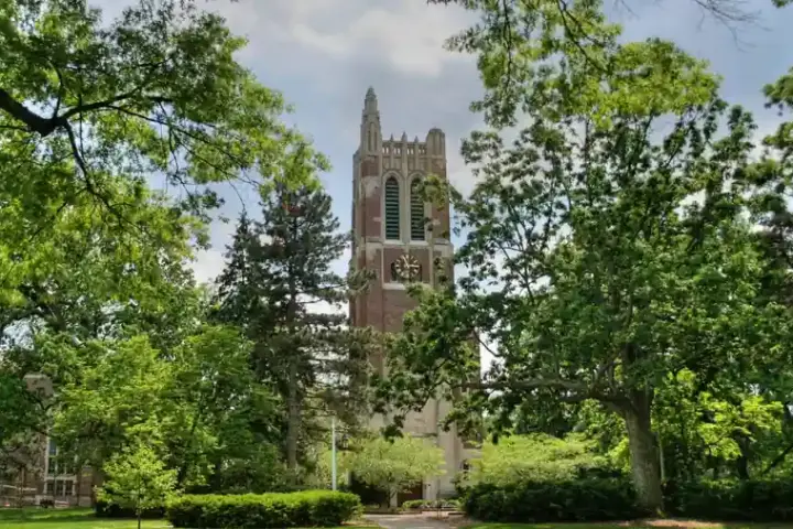 Brick clock and bell tower surrounded by trees and pathways on the Michigan State University campus in East Lansing.