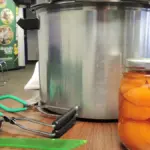 Open cans of peaches alongside canning supplies on a table.