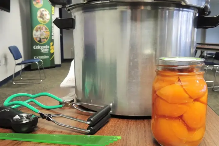 Open cans of peaches alongside canning supplies on a table.