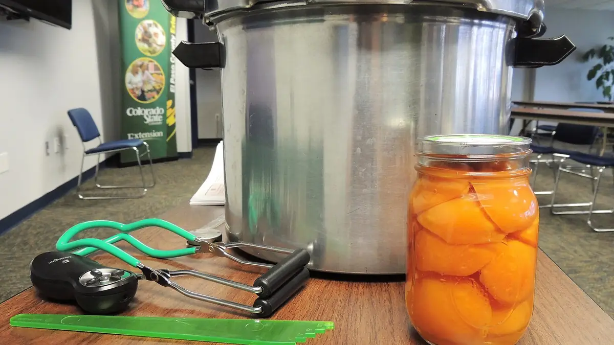 Open cans of peaches alongside canning supplies on a table.
