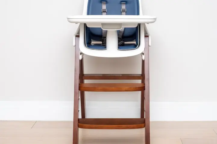A wooden high chair with a feeding tray in a bright room.