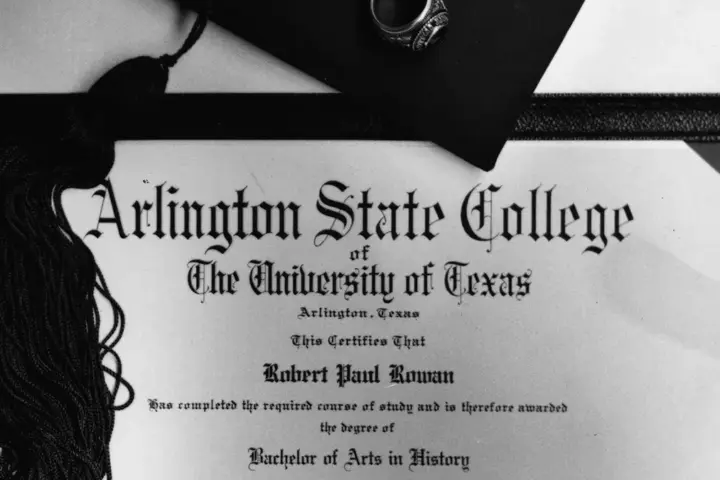 A formal university graduation diploma rolled with a ribbon alongside an academic graduation cap.