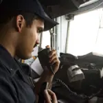 A large commercial vessel navigating open waters along the narrow shipping corridor of the Strait of Hormuz under naval escort.