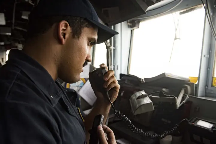 A large commercial vessel navigating open waters along the narrow shipping corridor of the Strait of Hormuz under naval escort.