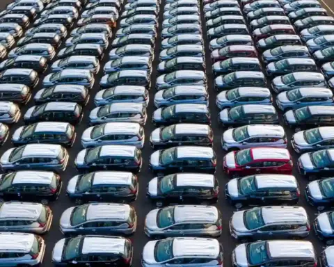 Rows of new cars parked in a large outdoor inventory lot viewed from above.