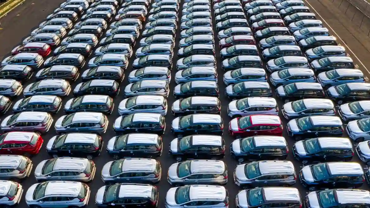 Rows of new cars parked in a large outdoor inventory lot viewed from above.