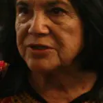 Close portrait of labor organizer Dolores Huerta speaking at a public event with a microphone and audience behind her.