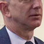 Formal portrait photograph of Amazon founder Jeff Bezos speaking during an official executive gathering.