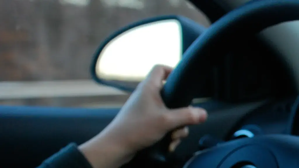 Close-up of a driver's hand gripping a steering wheel while driving, with blurred dashboard controls visible