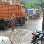 Motorists and pedestrians navigating waterlogged roads under monsoon rain in southern India.