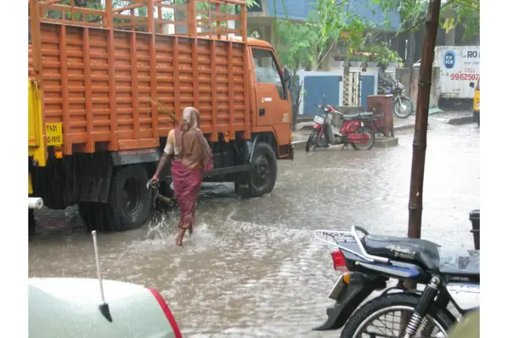 Motorists and pedestrians navigating waterlogged roads under monsoon rain in southern India.