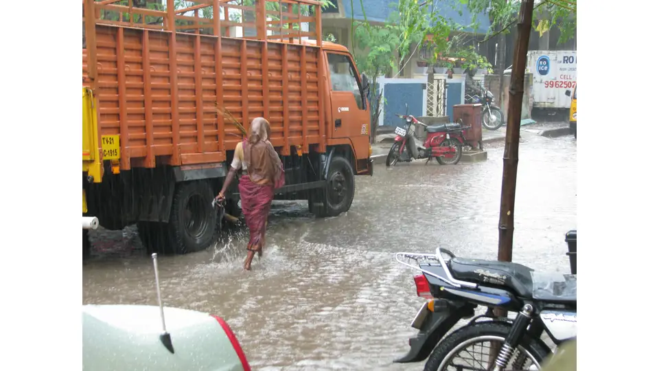 Motorists and pedestrians navigating waterlogged roads under monsoon rain in southern India.