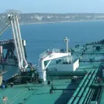 A large crude oil tanker unloading cargo at an industrial port, representing the class of vessel struck in the Strait of Hormuz