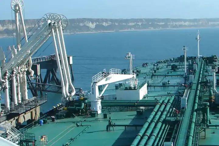 A large crude oil tanker unloading cargo at an industrial port, representing the class of vessel struck in the Strait of Hormuz